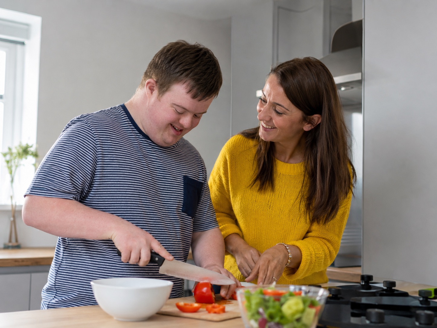 A support worker and a young man preparing a meal together in a kitchen.